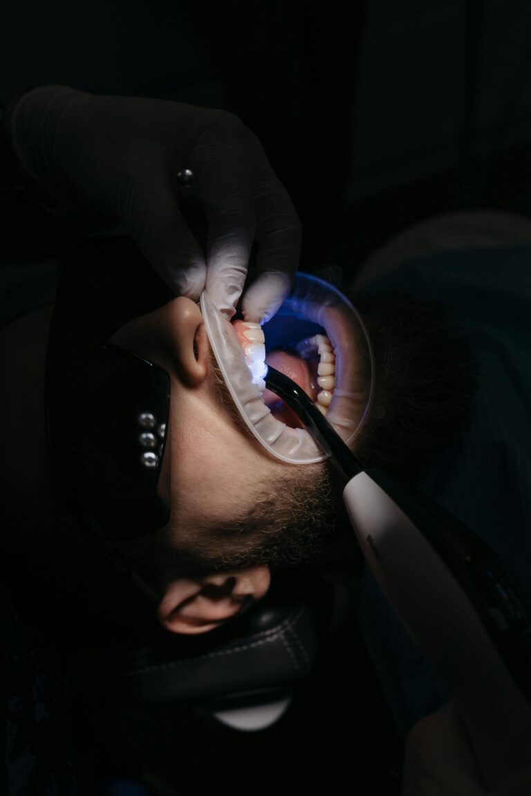 Primer plano oscuro de una boca abierta siendo examinada con luz y herramientas dentales