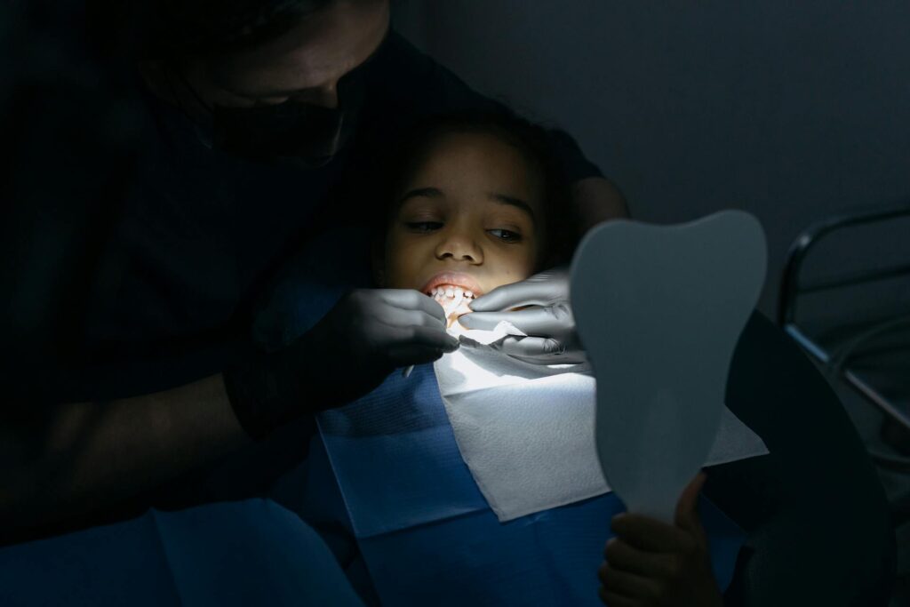 Niño pequeño recostado en el sillón dental siendo examinado por un dentista con luz focalizada