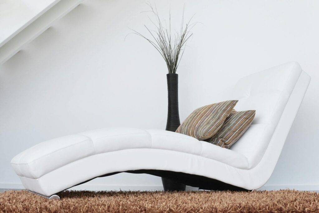 Diván o chaise lounge de diseño moderno blanco y curvo junto a un jarrón negro alto con ramas secas