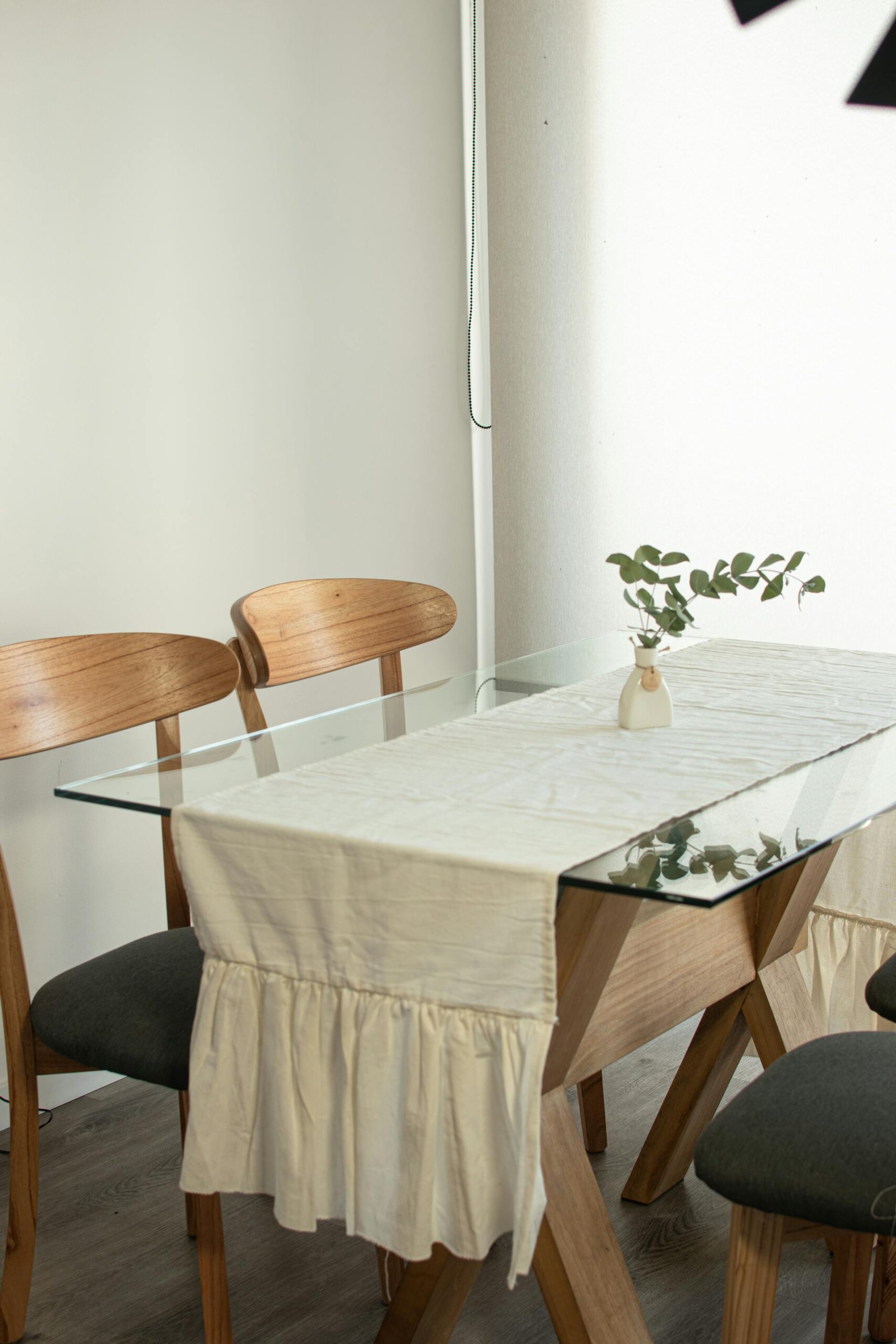 Detalle de mesa de comedor vestida con mantel color crema y camino de mesa, con sillas de madera