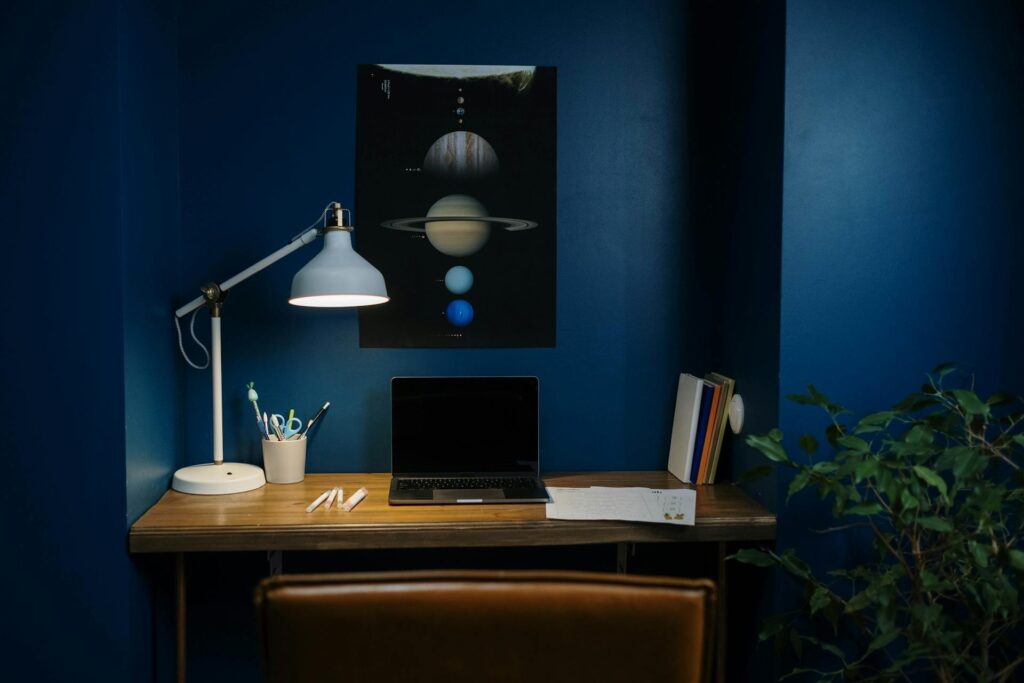 Oficina en casa con paredes azul oscuro, escritorio de madera, lámpara de mesa y póster espacial