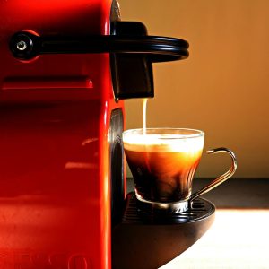 Maquina de café expreso roja sirviendo café en taza de vidrio