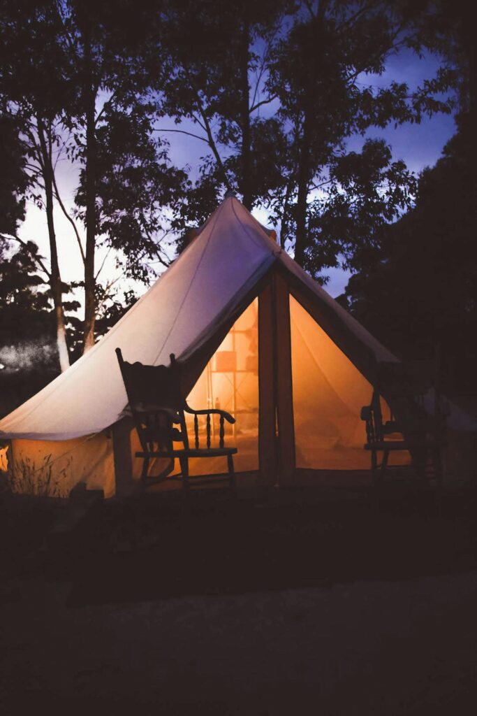 Tienda de campaña grande estilo "bell tent" con luz cálida en medio de un bosque