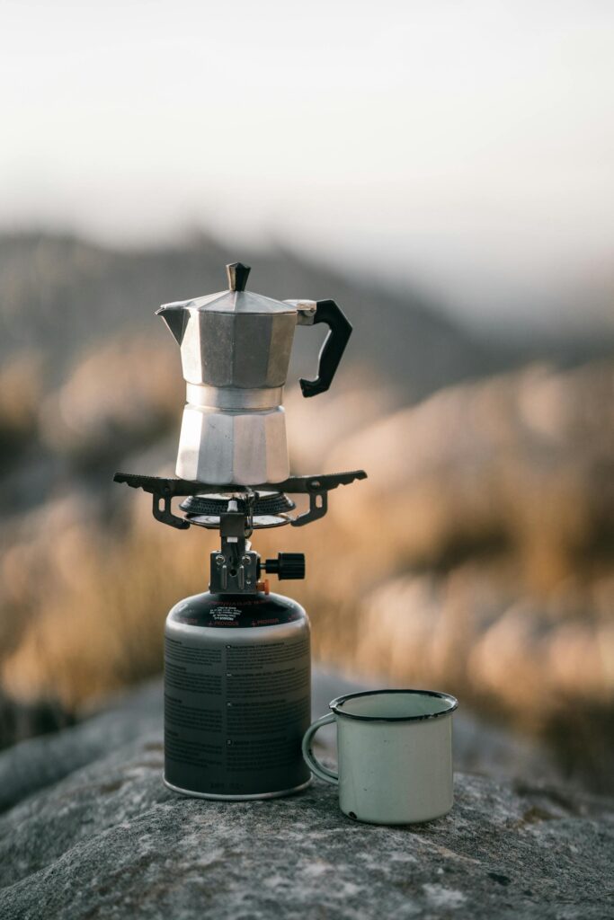 Cafetera colocada sobre un hornillo de gas portátil con montañas de fondo