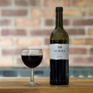 Botella de vino con etiqueta azul oscuro y copa pequeña