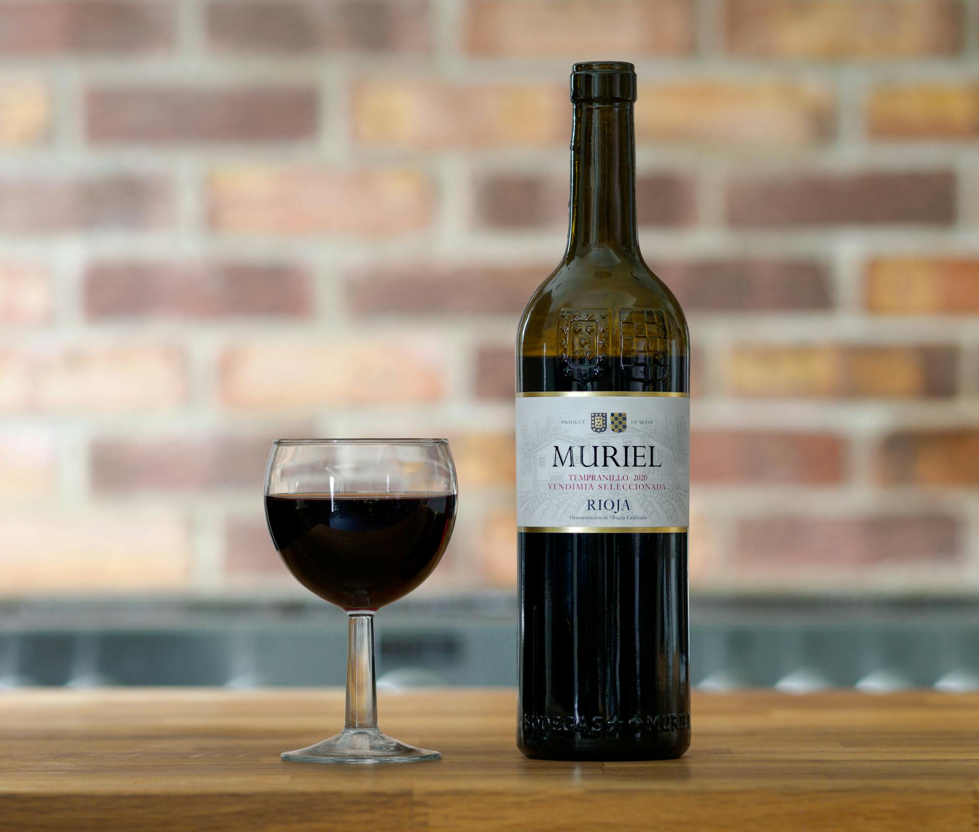 Botella de vino con etiqueta azul oscuro y copa pequeña