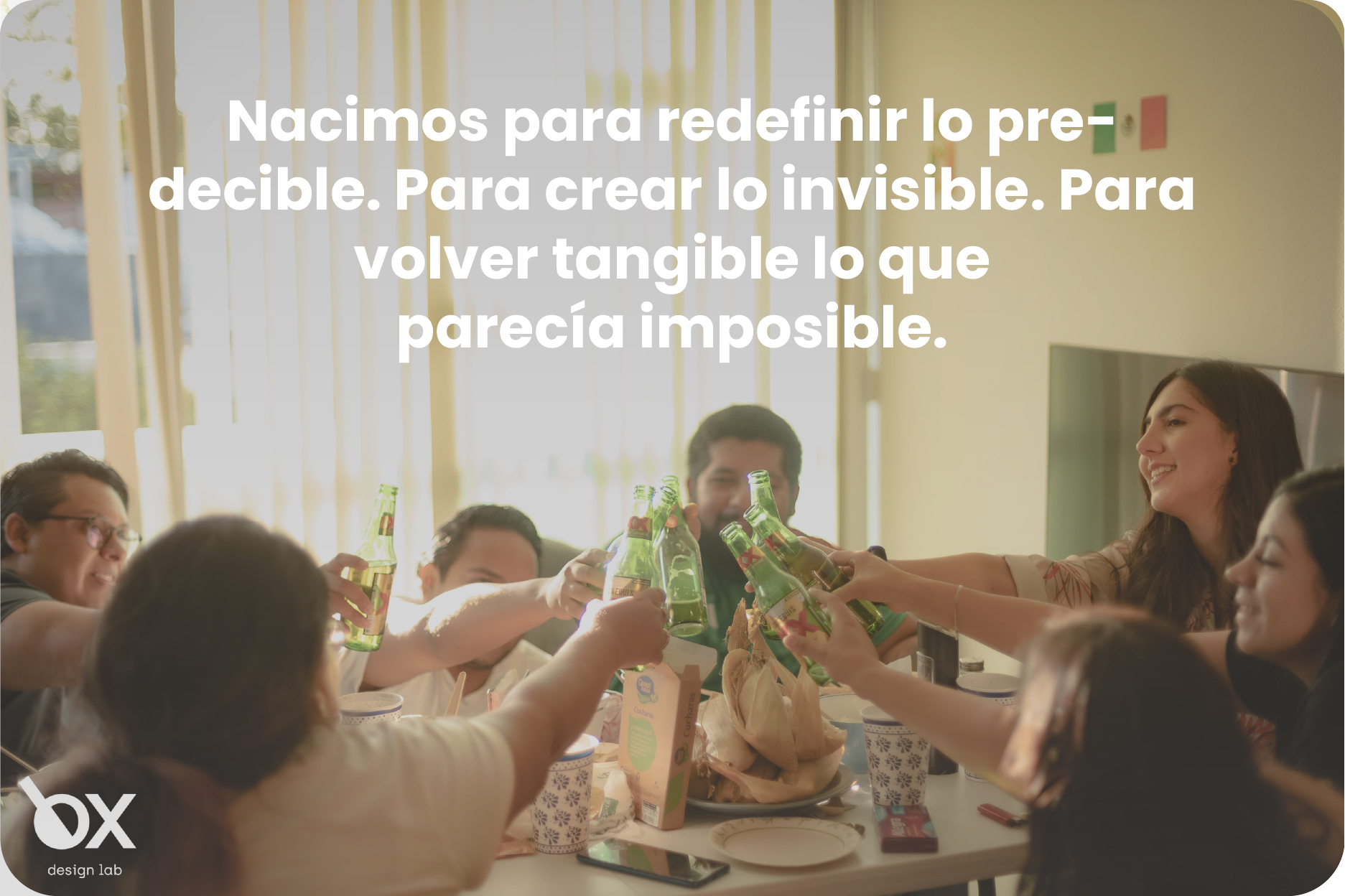 "Grupo de personas alrededor de una mesa haciendo un brindis con botellas, con un texto superpuesto que dice: 'Nacimos para redefinir lo predecible. Para crear lo invisible. Para volver tangible lo que parecía imposible'