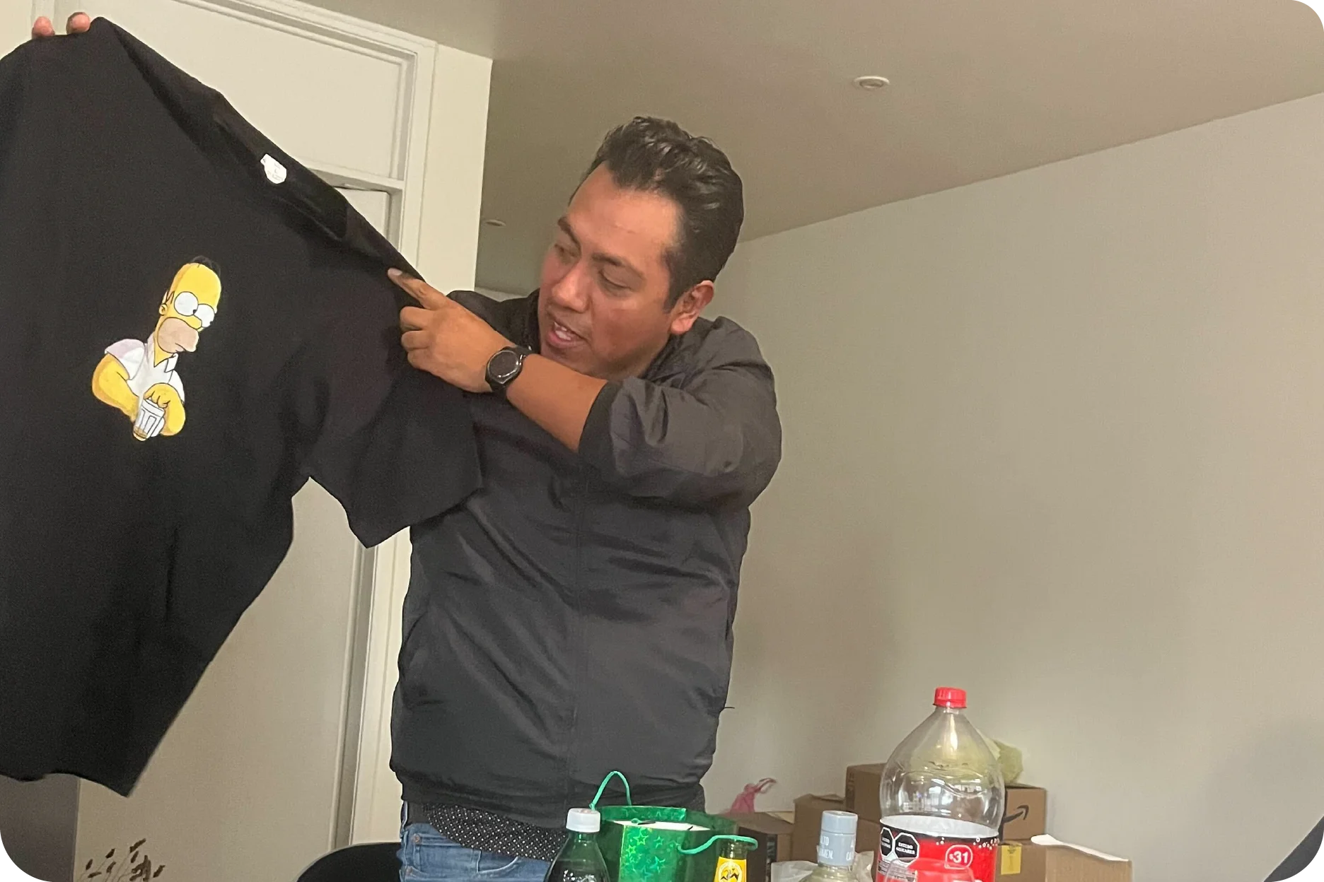 Miembro del equipo recibiendo un regalo divertido: una playera con un diseño de caricatura durante una celebración informal.